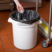 A white Baker's Mark 20 gallon round ingredient storage bin with a black liner, shown in a commercial kitchen setting.