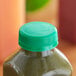 A green juice bottle with a green unlined tamper-evident cap on a table.