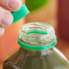 A hand using a green unlined tamper-evident cap to close a bottle of green liquid.