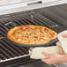 A person using an oven mitt to remove a pizza from a Tablecraft cast iron pizza pan.