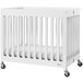 A Foundations Boutique white slatted wood folding crib with wheels.