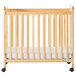 A natural wood slatted crib with wheels and mattress.