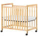 A natural wood Foundations SafetyCraft crib with clearview sides and wheels.
