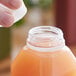A hand pouring orange juice into a plastic bottle with a clear tamper-evident cap.