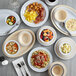 A set of small, bone white, smooth melamine ramekins displayed among various plates and bowls of food.