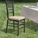 A Lancaster Table & Seating black wood Chiavari chair with a gold cushion on a grassy field.