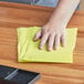 A person using a yellow Lavex dusting cloth to clean a table.