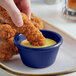 A person dipping a chicken finger into a blue bowl of sauce.