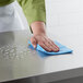 A hand using a Lavex blue general purpose wiper to clean a stainless steel countertop.