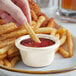 A person dipping a french fry into a white Acopa ramekin filled with ketchup.