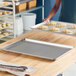 A metal perforated baking sheet pan sits on a wooden countertop, with another similar pan holding unbaked croissants in the background.