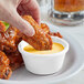 A hand dipping a chicken wing into a white Acopa ramekin of sauce.
