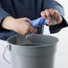 A person in a blue uniform using a blue Schama towel to clean a bucket in a professional kitchen.