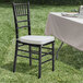 A Lancaster Table & Seating black wood Chiavari chair with ivory cushion on a grass field.