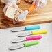 A Choice stainless steel sandwich spreader with a neon pink handle being used to spread spread on a piece of bread.