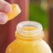 A hand holding a plastic bottle of orange juice with an unlined orange tamper-evident cap.