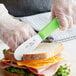 A person using a Choice Scalloped Stainless Steel Sandwich Spreader to cut a sandwich.