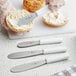 A Choice stainless steel sandwich spreader with a white handle spreading cream on a bagel.