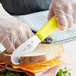 A person using a Choice stainless steel sandwich spreader to cut a sandwich.
