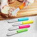 A Choice stainless steel sandwich spreader with a neon yellow handle being used to spread food on a piece of bread.