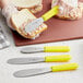 A Choice stainless steel sandwich spreader with a neon yellow handle being used to spread food on a sandwich.