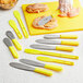 A Choice stainless steel sandwich spreader with a yellow polypropylene handle on a counter.