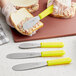 A Choice stainless steel sandwich spreader with a yellow handle being used to spread food on a piece of bread.