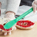 A gloved hand uses a green Choice sandwich spreader to spread jam on a bagel.