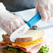A person using a Choice scalloped sandwich spreader to cut a sandwich.