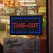 A rectangular LED sign that says "Take Out" on a counter in a pizza parlor.