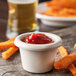 A Carlisle ivory bone melamine ramekin filled with ketchup next to a plate of french fries on a table.
