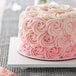 A white square cake board with a cake decorated with pink frosting and roses on top.