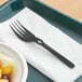 A black WeGo polystyrene fork on a napkin next to a bowl of fruit.