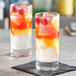 Two Pasabahce highball glasses of fruit juice with ice and raspberries.