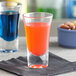 A Pasabahce Boston shooter glass filled with blue liquid on a table with nuts.