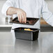A chef using a Cambro black plastic container with a black handled lid to put food in it.