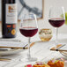 An Acopa Radiance wine glass filled with red wine on a table set with food.
