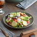An Acopa moss green matte coupe stoneware plate with a salad on a wooden table.