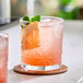 A pink beverage with ice, a citrus slice, and mint leaves served in an 11 oz. Acopa Gardenia rocks glass.