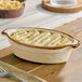 An oval-shaped, vanilla bean-colored porcelain baker or casserole dish with a brown rim, holding a baked dish.