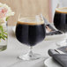 Two Acopa Covella brandy snifter glasses of dark liquid on a table with flowers.