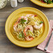 A Capri citrus yellow stoneware plate with shrimp and noodles on it on a table.