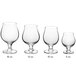 A row of six clear Acopa Select tulip glasses with white liquid in one.