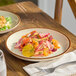 An Acopa Keystone 8 1/2 inch vanilla bean porcelain coupe plate with a colorful salad served on it.