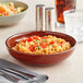 An Acopa Keystone Sedona Orange stoneware low bowl filled with rice and tomatoes on a table with a knife and fork.