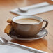 A brown matte stoneware cup filled with coffee, served on a matching saucer with two biscotti pieces.