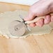 A hand uses an Ateco stainless steel pastry cutter with a wood handle to cut dough.