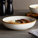 Two Acopa Keystone vanilla bean stoneware coupe low bowls filled with food on a table.