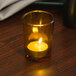 A Sterno Petite Amber Votive Glass candle on a table in a dark room.