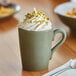 An Acopa moss green stoneware mug filled with coffee and topped with whipped cream and sprinkles.